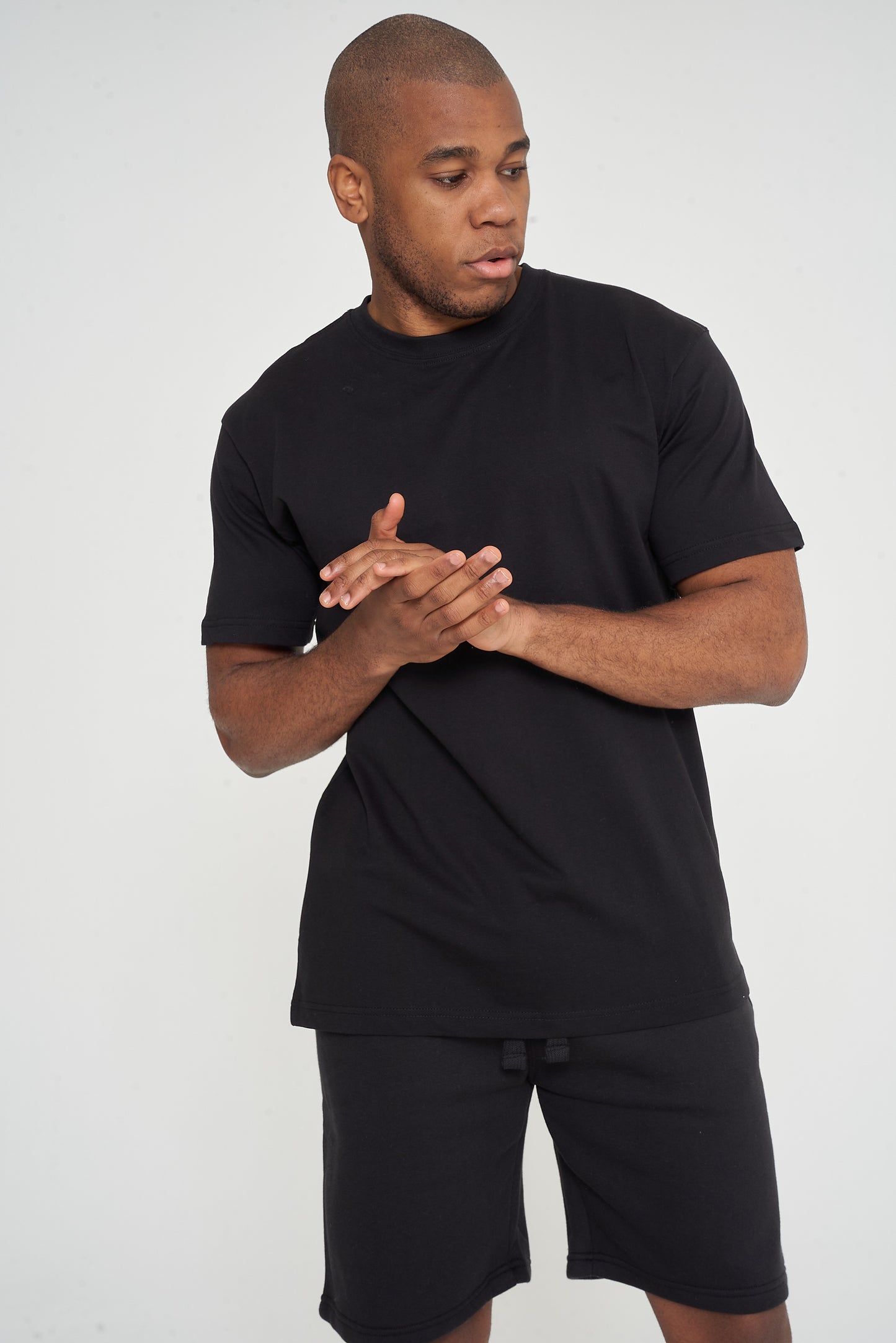 Male model adjusting sleeves in black 365 Oversized T-shirt and shorts – oversized fit, 365 Collection.