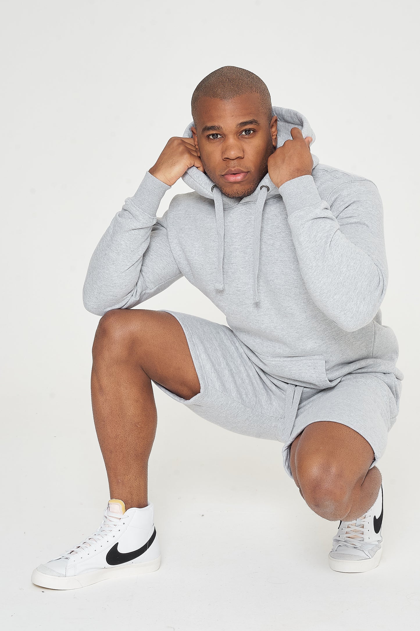 Male model seated wearing grey regular fit hoodie and shorts, showing casual street style - 365 Collection.