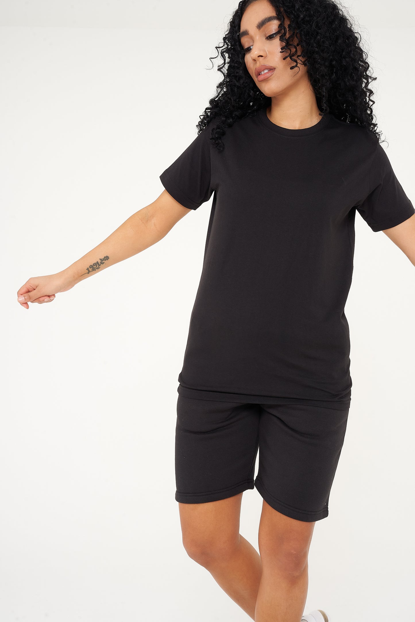 A woman dressed in a black t-shirt and shorts, in a casual pose to showcase fit and comfort.