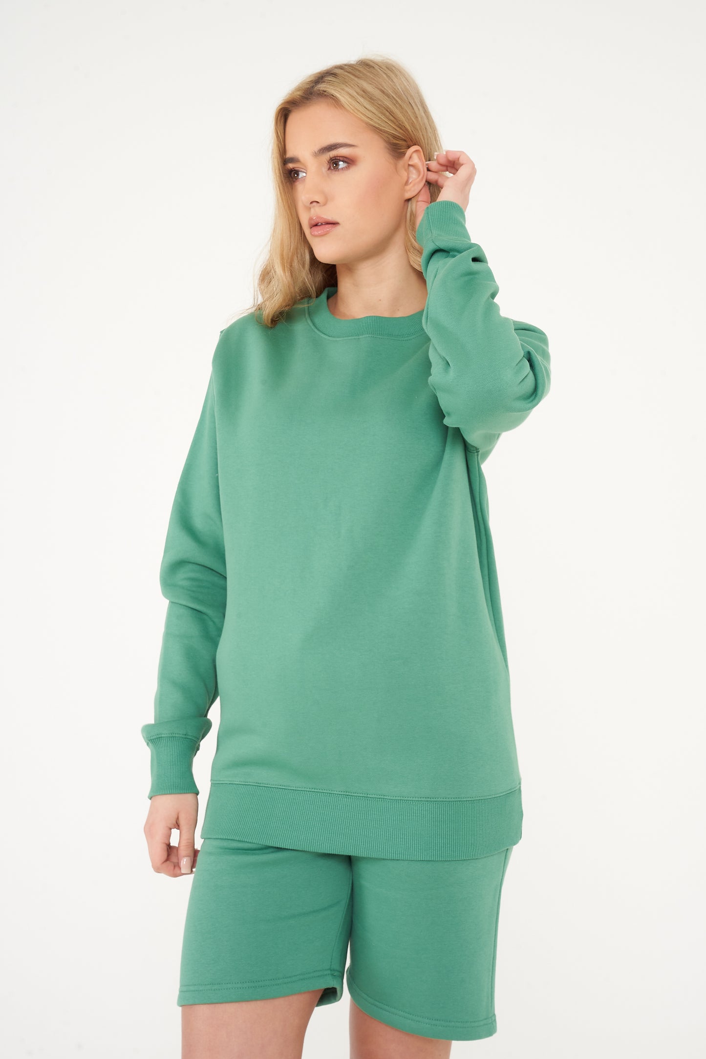 Woman standing in green sweatshirt and shorts, casual pose displaying color and minimalist style.