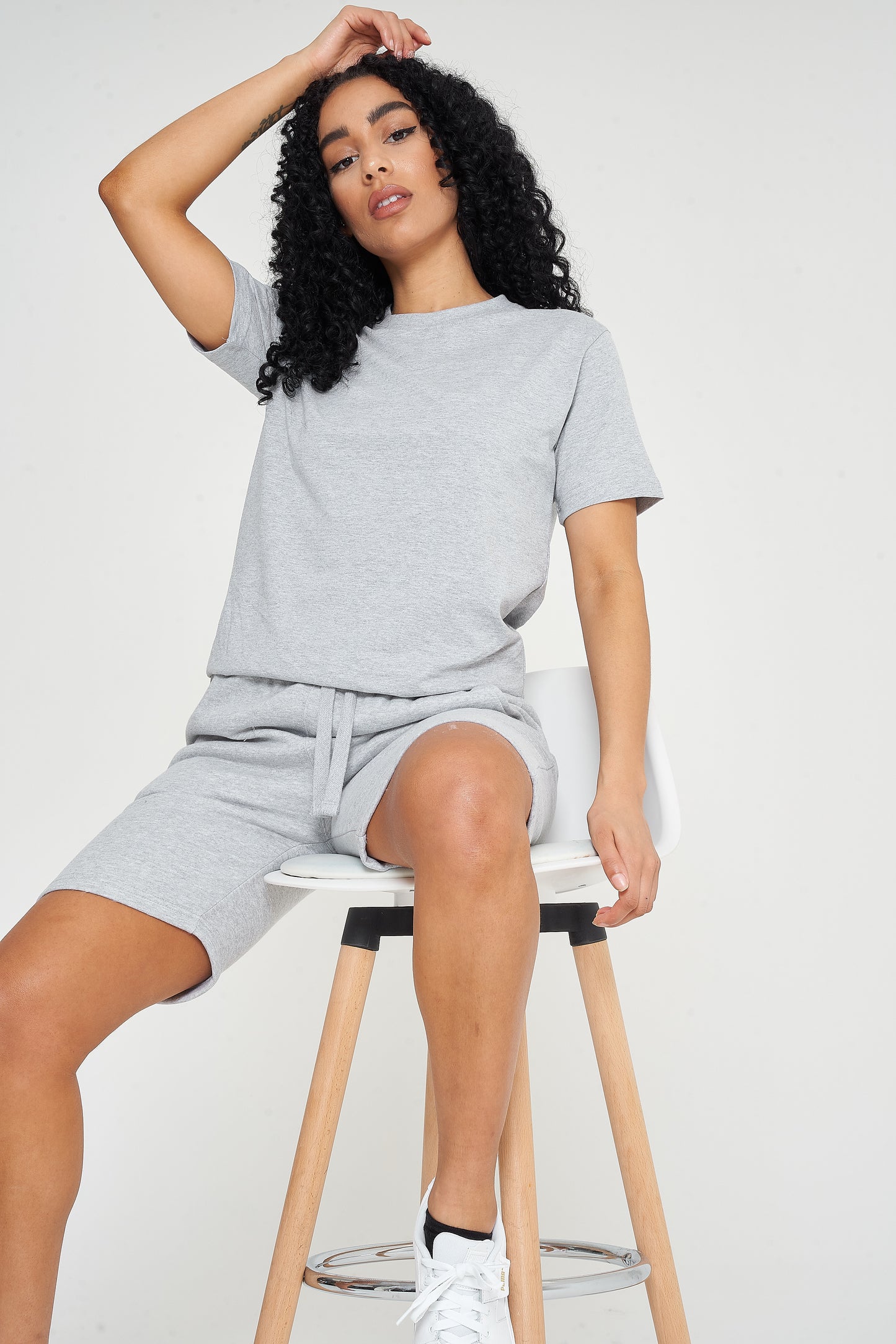 A woman in grey shorts and a t-shirt, sitting on a stool, displaying casual style and comfort.