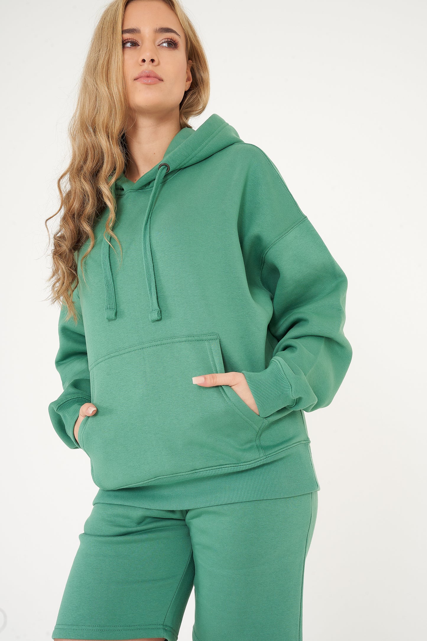 Side view of a woman in an oversized green hoodie and shorts, showing relaxed fit and ribbed cuffs.