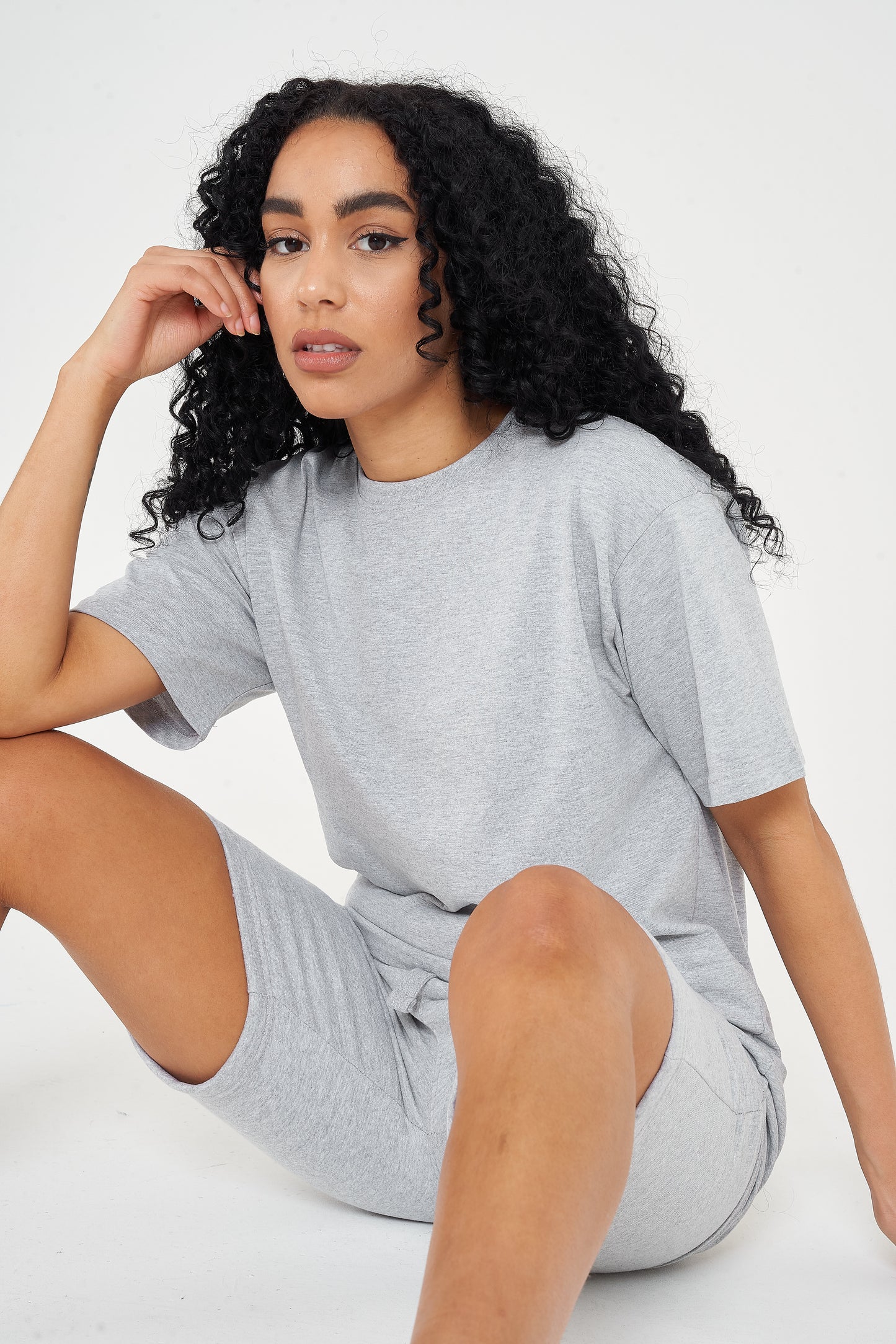 Woman in oversized grey cotton t-shirt and shorts, seated casual pose, displaying a modern fit.