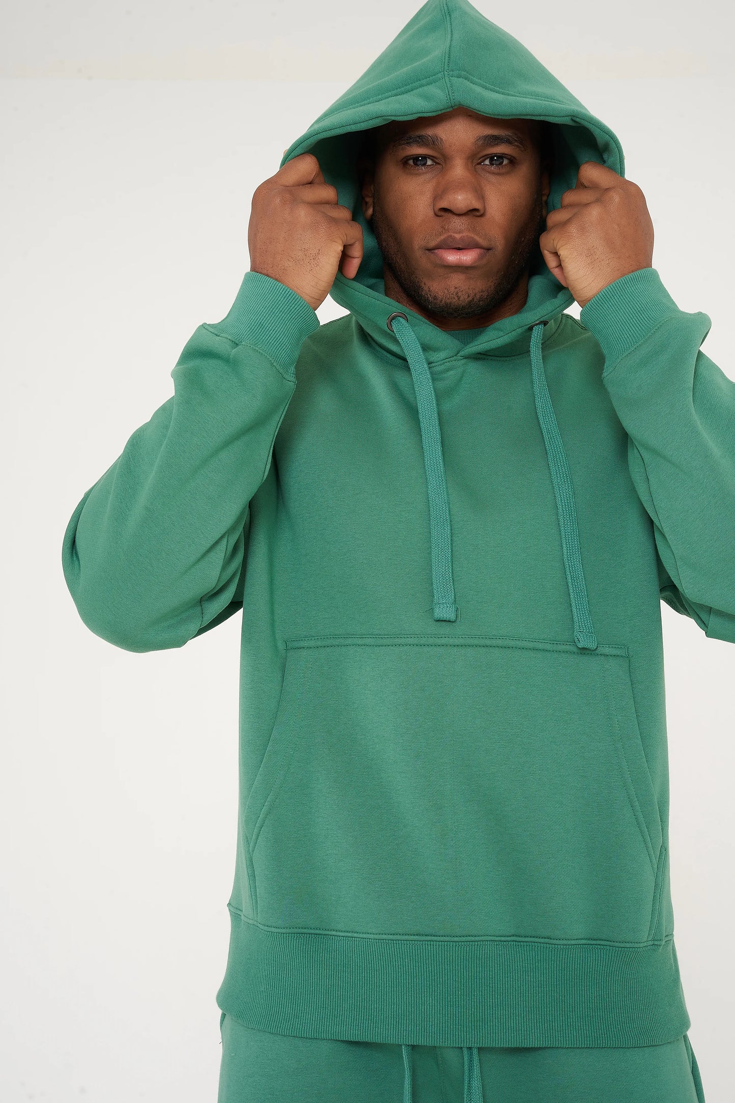 Male model adjusting hood on green oversized hoodie and shorts - 365 Collection.