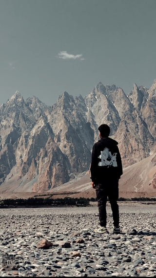 A person standing on a rocky plain, facing majestic mountain peaks under a clear sky - ideal for themes highlighting outdoor exploration, adventure, or scenic travel.