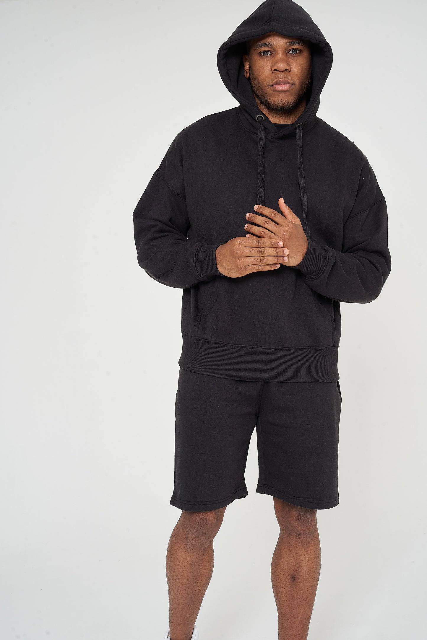 Male model side angle wearing black 365 Oversized Hoodie with hood up and shorts – oversized fit, 365 Collection.