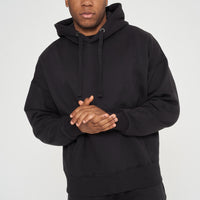 Male model front view standing, hands clasped, in black 365 Oversized Hoodie and shorts – oversized fit, 365 Collection.