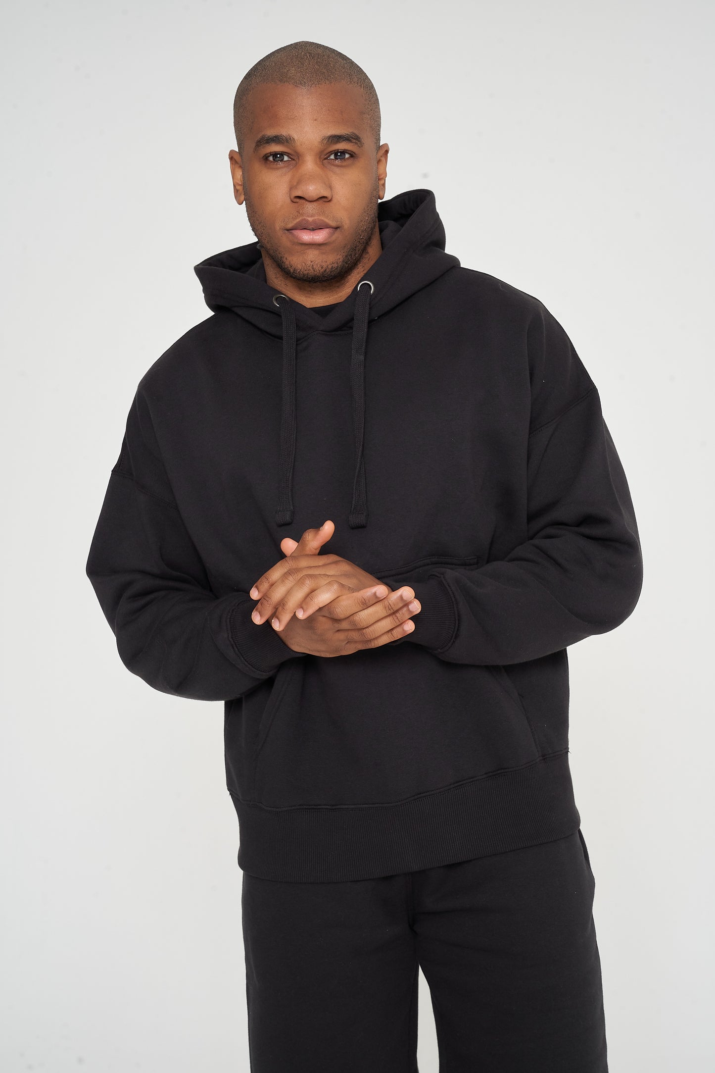 Male model front view standing, hands clasped, in black 365 Oversized Hoodie and shorts – oversized fit, 365 Collection.