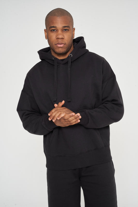 Male model front view standing, hands clasped, in black 365 Oversized Hoodie and shorts – oversized fit, 365 Collection.