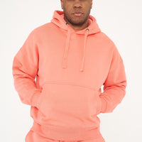 Male model standing in coral 365 Oversized Hoodie and shorts with hands in pockets, relaxed posture – 365 Collection – oversized fit. 