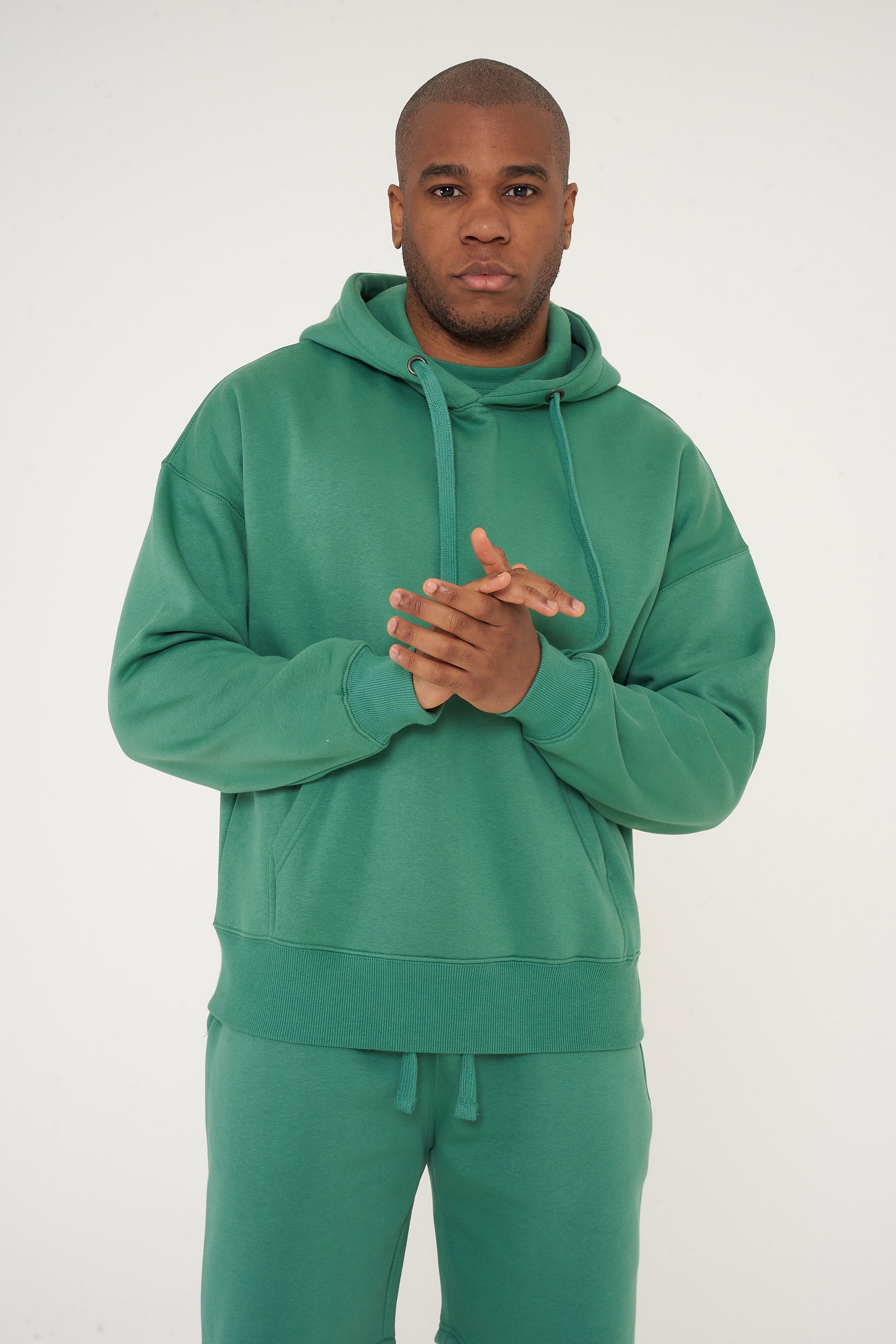 Male model front-facing in green oversized hoodie and shorts, hands relaxed - 365 Collection.