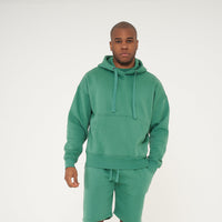 Full-body front view of a male model wearing a green oversized hoodie and shorts - 365 Collection.
