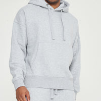 Upper body view of model wearing grey oversized hoodie with hands in pocket - 365 Collection.