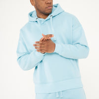 Model posing with clasped hands in turquoise oversized hoodie - 365 Collection.