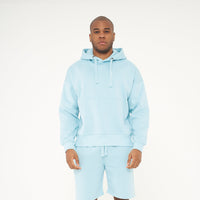 Full-body front view of model wearing men’s turquoise oversized hoodie - 365 Collection. 