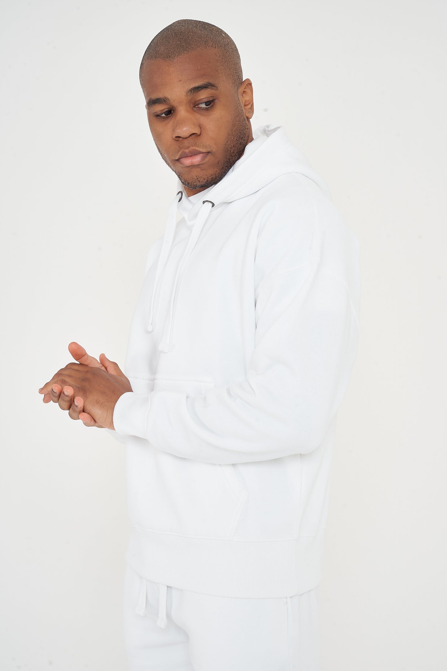 Model posing in men's white oversized hoodie with hands clasped, 365 Collection.
