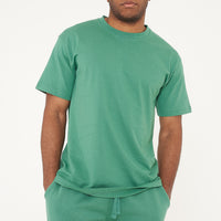Male model front-facing in green oversized T-shirt and shorts, hands relaxed - 365 Collection.
