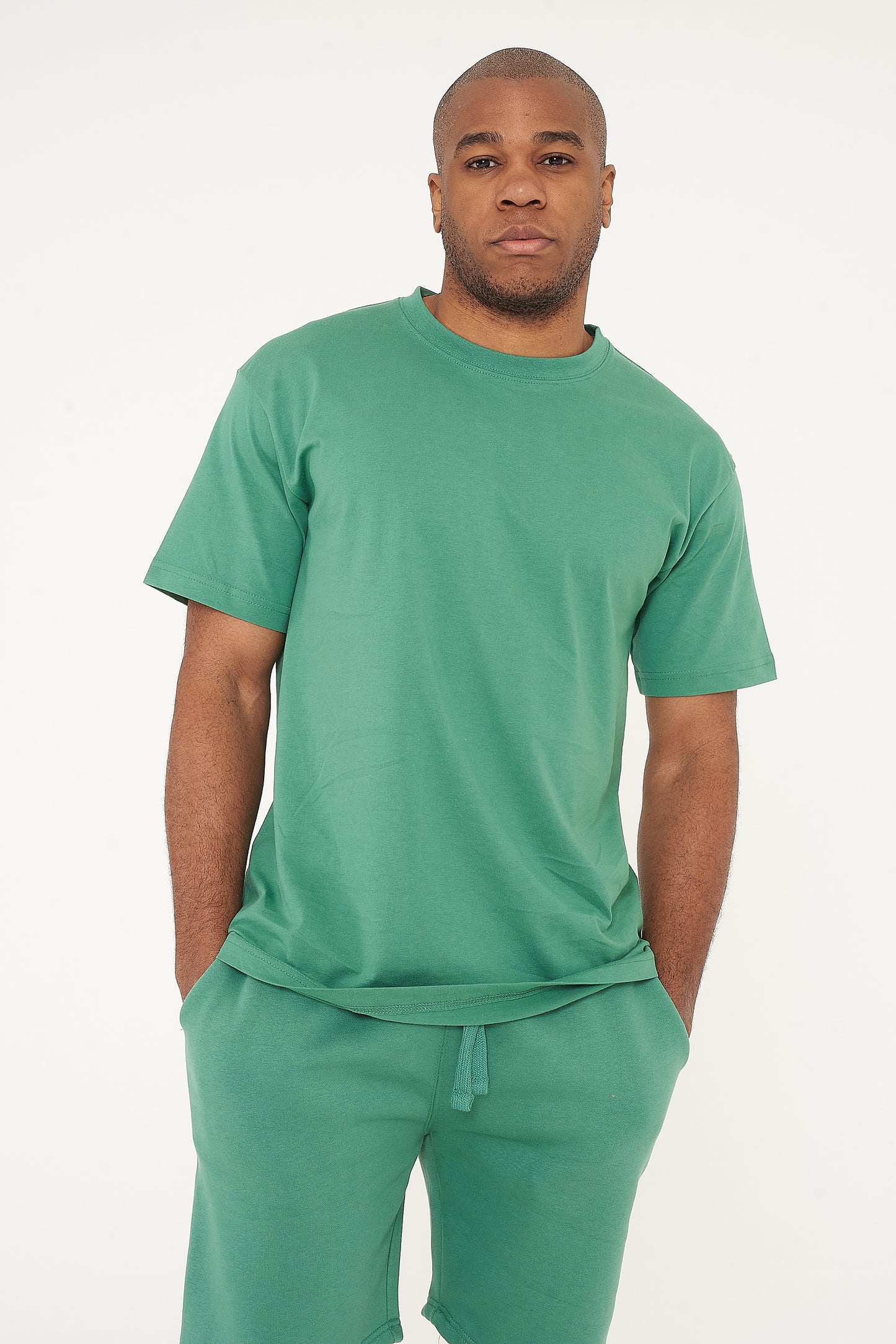 Male model front-facing in green oversized T-shirt and shorts, hands relaxed - 365 Collection.