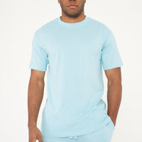 Model in men's turquoise oversized T-shirt with one hand in pocket, 365 Collection.