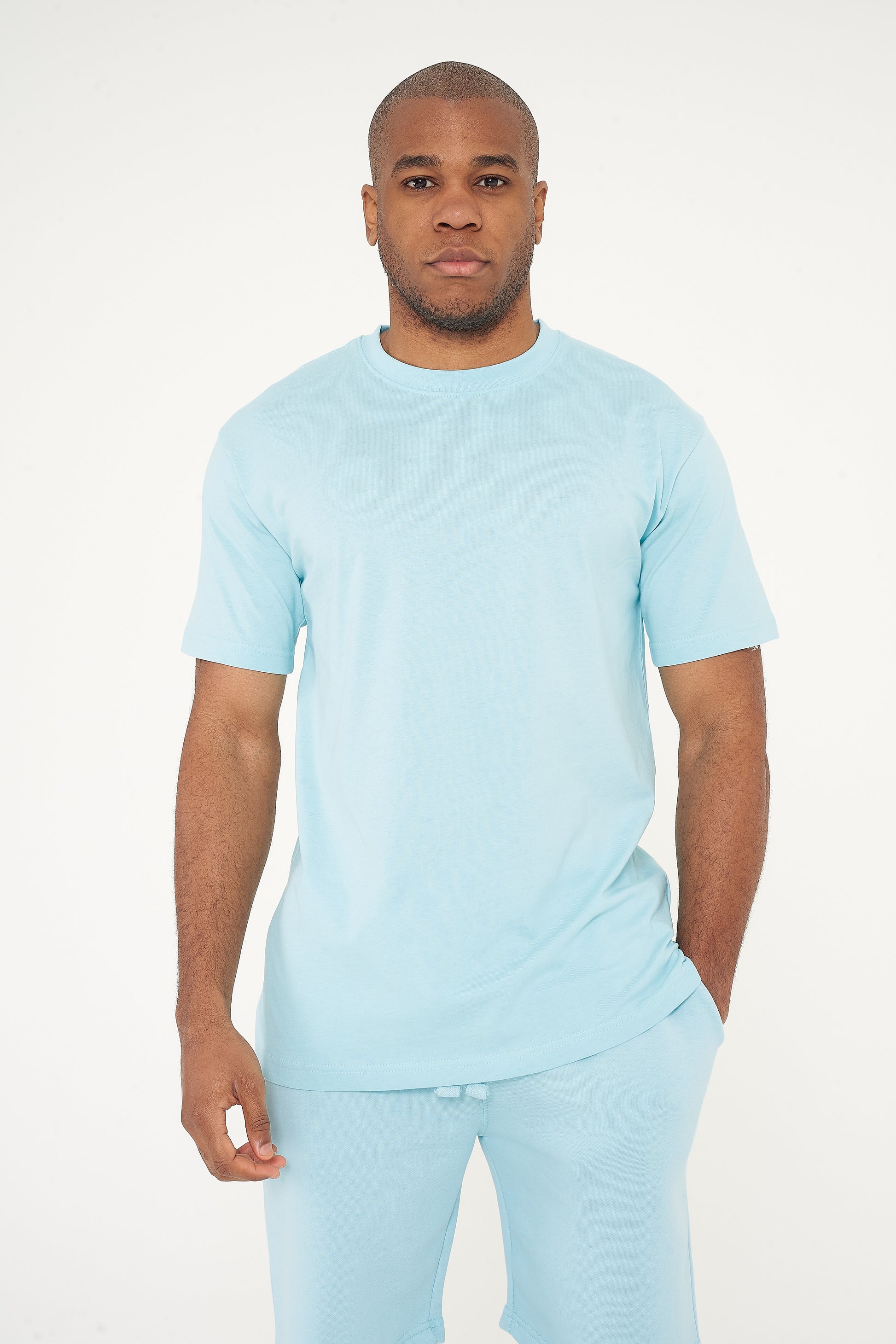 Model in men's turquoise oversized T-shirt with one hand in pocket, 365 Collection.