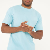 Model posing in men's turquoise oversized T-shirt with hands clasped together, 365 Collection.