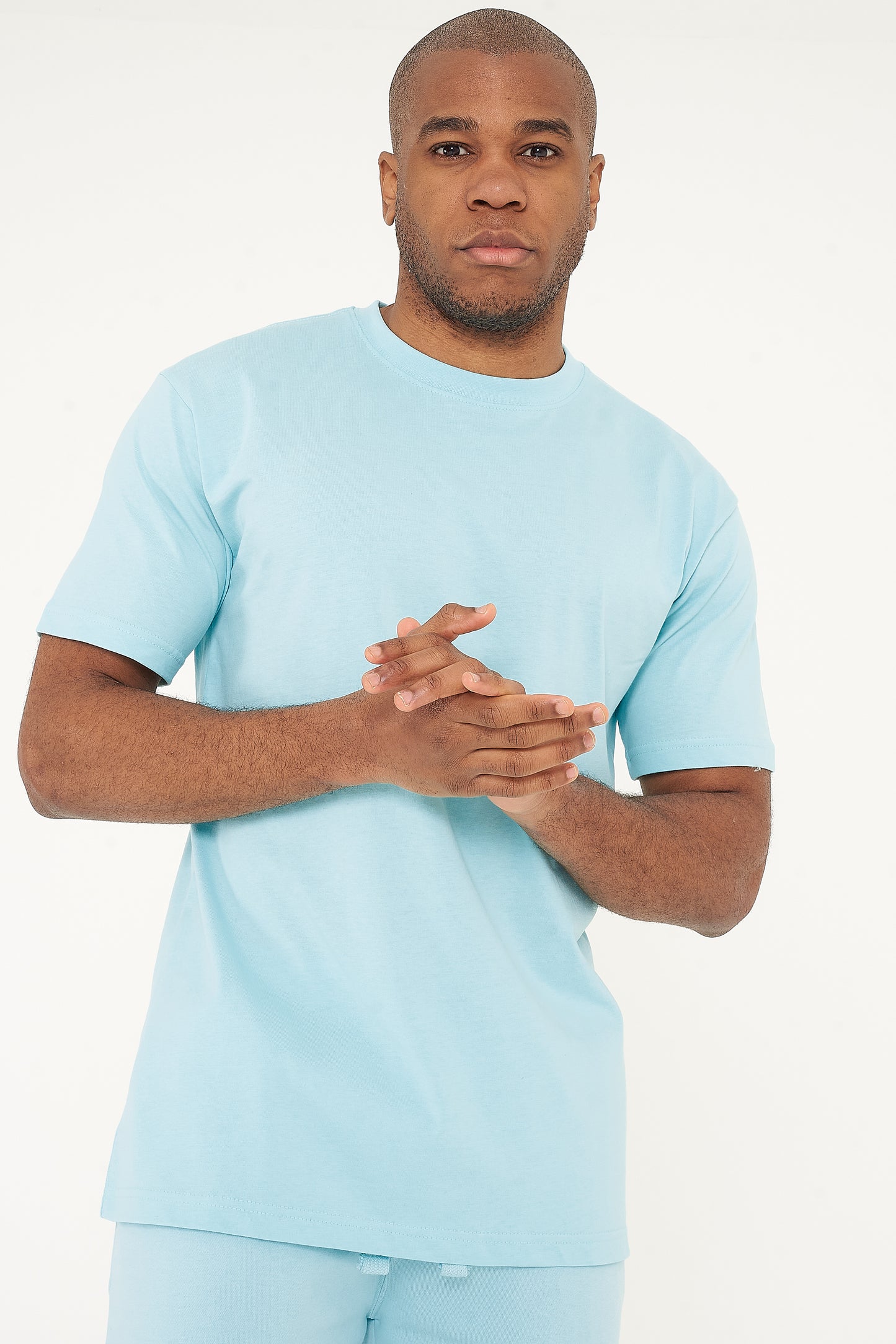 Model posing in men's turquoise oversized T-shirt with hands clasped together, 365 Collection.