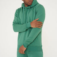 Male model adjusting the sleeve of green regular fit hoodie and shorts – 365 Collection.