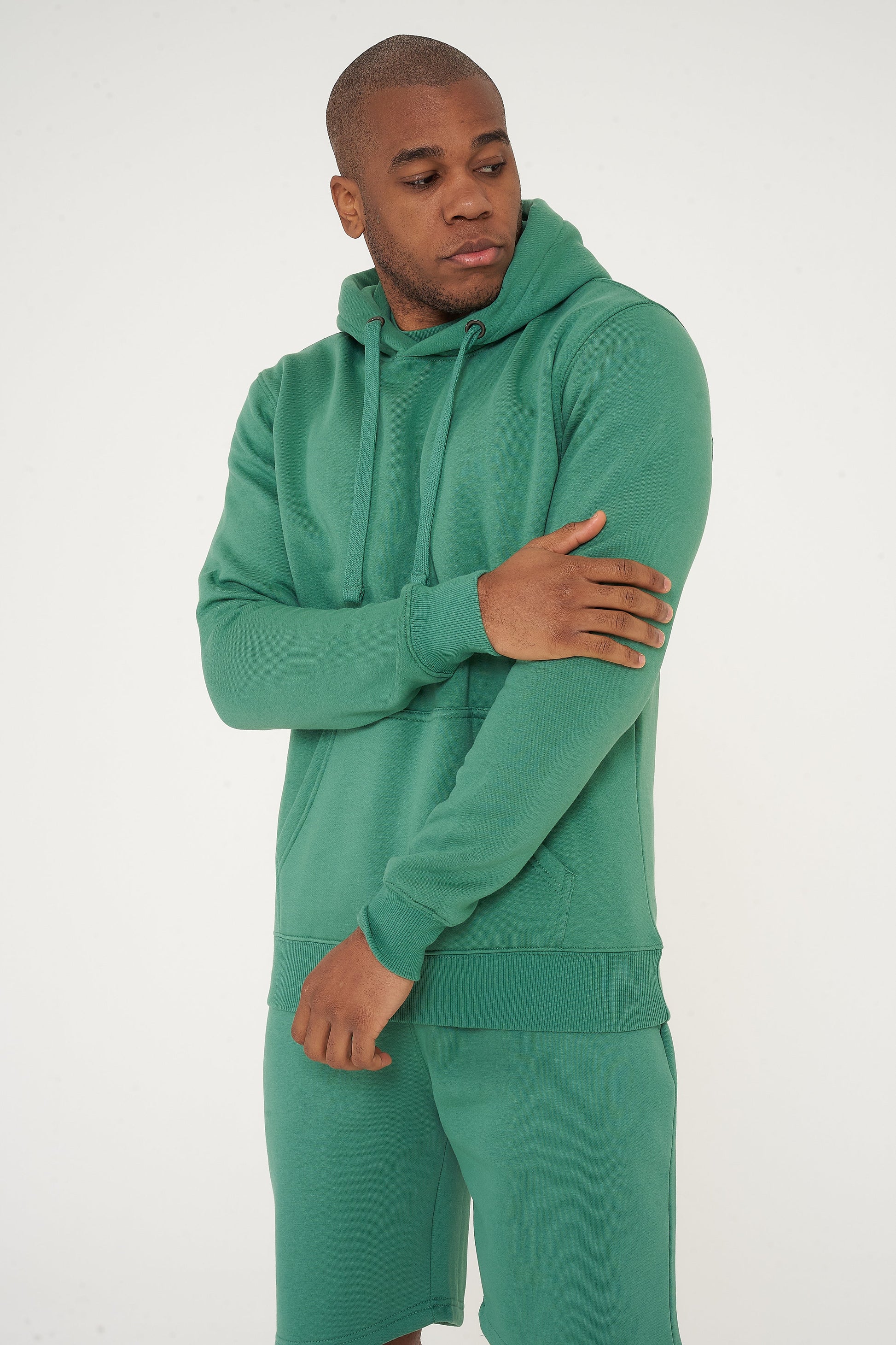 Male model adjusting the sleeve of green regular fit hoodie and shorts – 365 Collection.