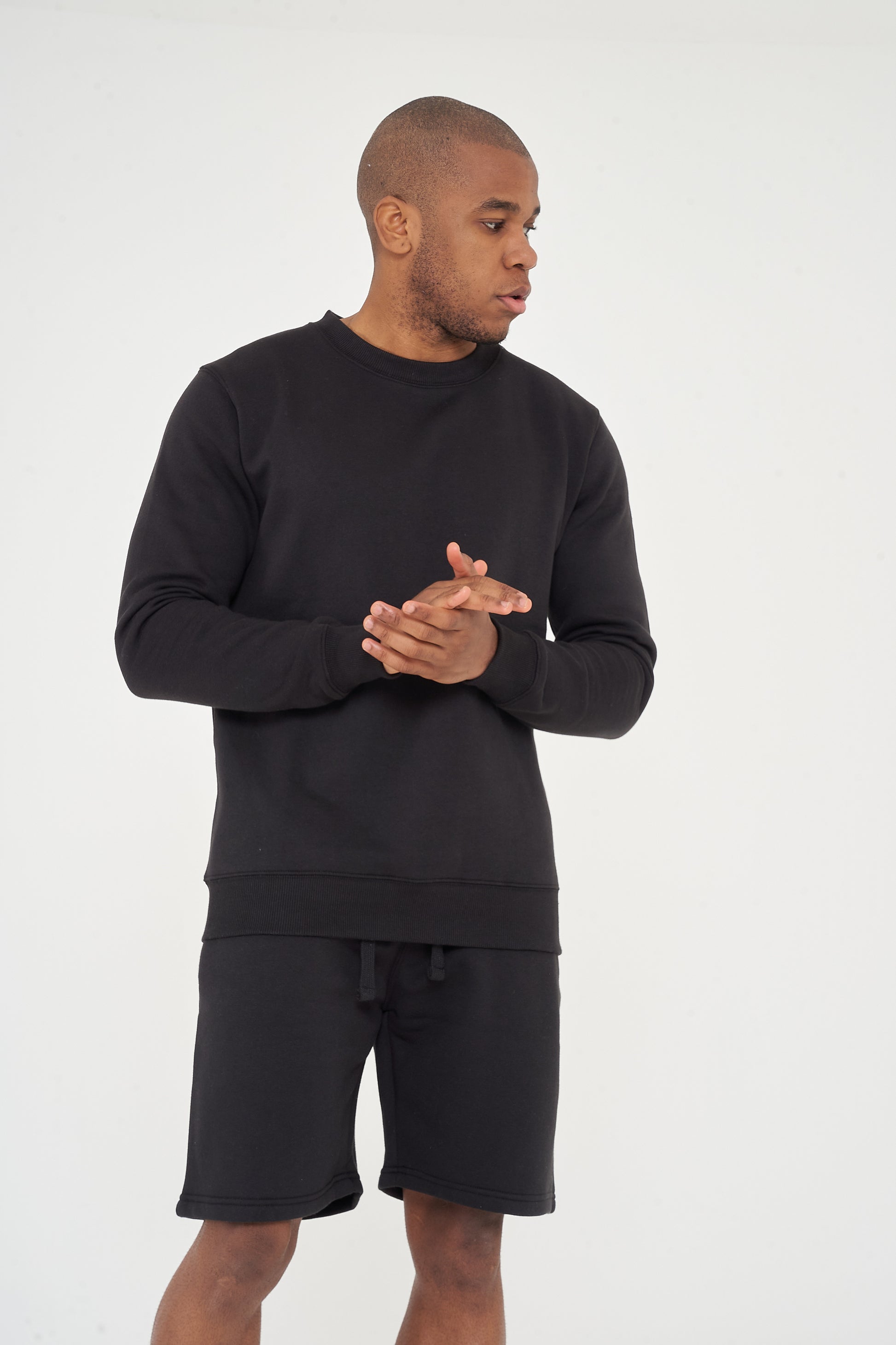 Male model front view wearing black 365 Regular Sweatshirt and matching shorts, hands clasped – regular fit, 365 Collection.