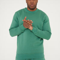 Model front-facing in green regular fit sweatshirt and shorts, hands clasped - 365 Collection.