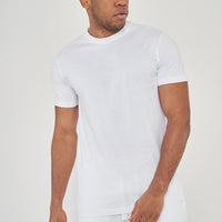 Man wearing a plain white t-shirt and white pants, standing against a light background.