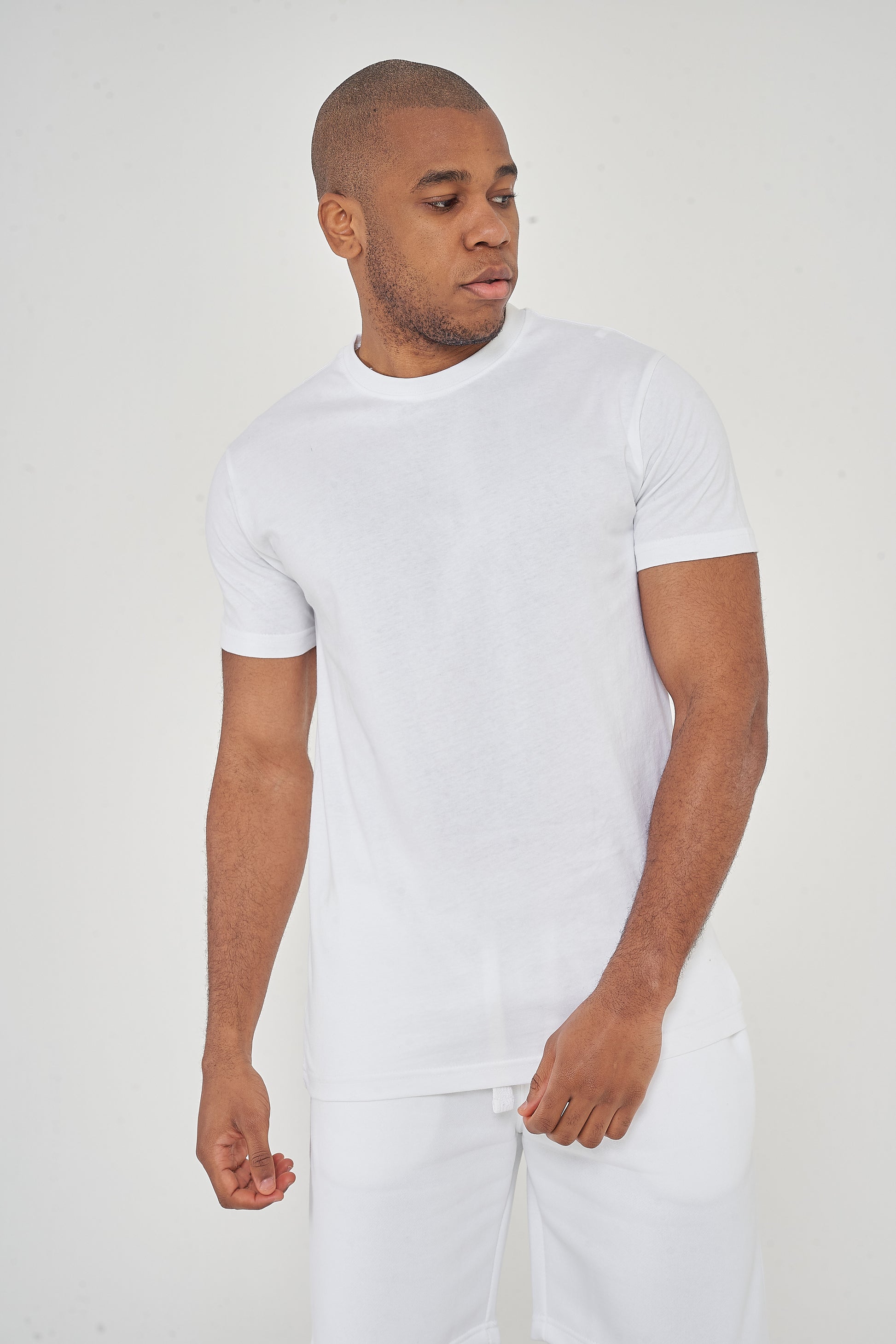 Man wearing a plain white t-shirt and white pants, standing against a light background.