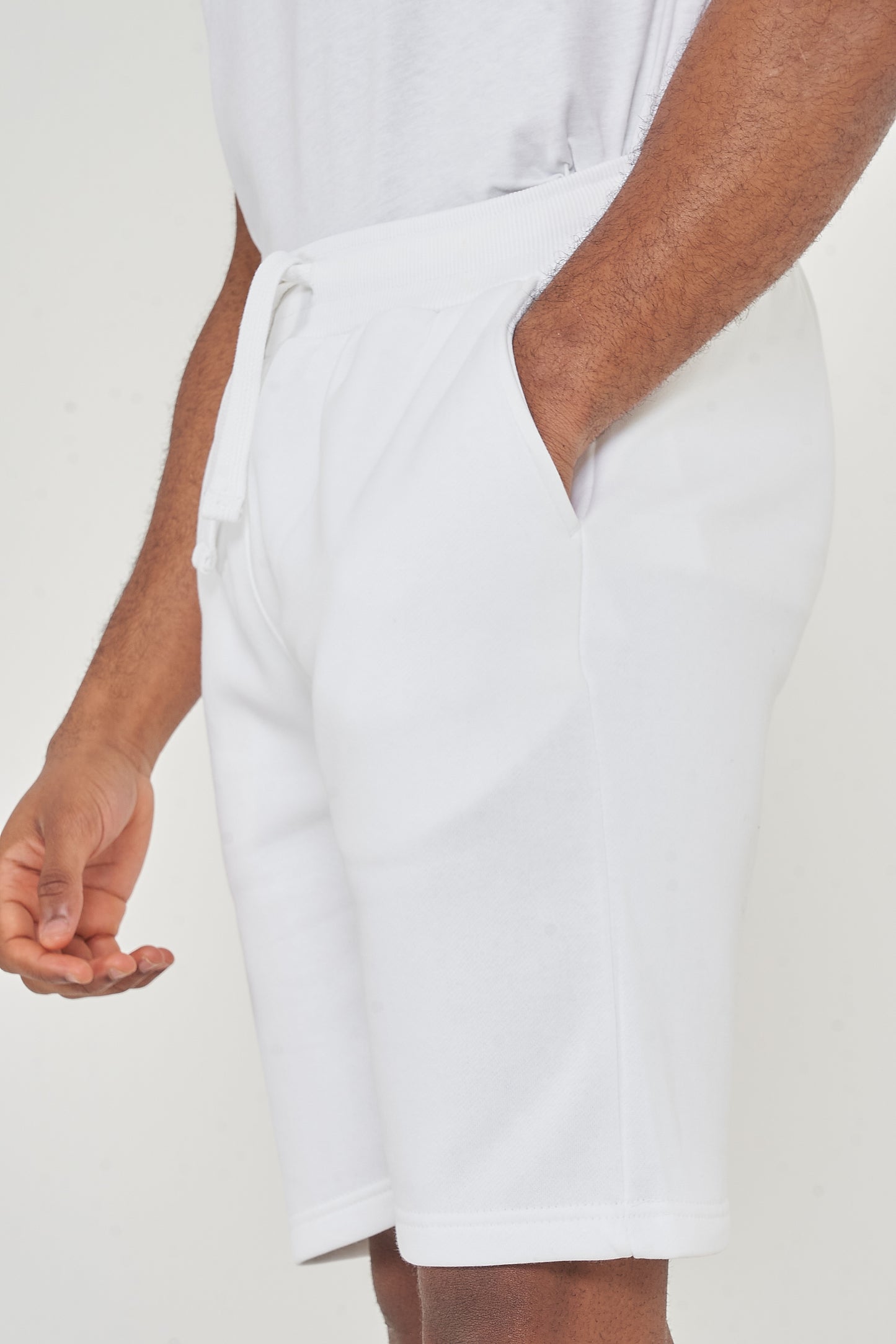 Side view of model wearing men's white shorts with one hand in pocket, 365 Collection.