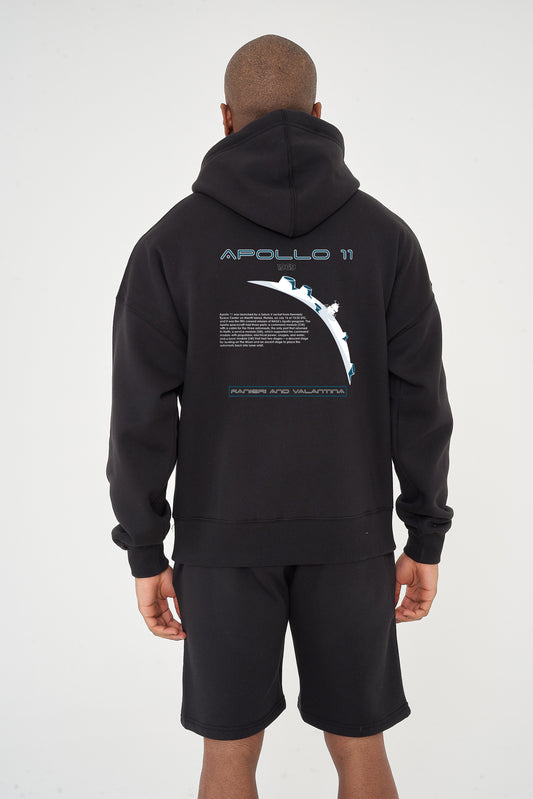 Rear view of male model wearing black Apollo 11 Oversized Hoodie with Apollo 11 graphic, paired with black shorts – oversized fit.