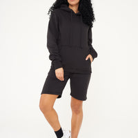 A woman in a black basic hoodie paired with shorts, standing in a casual pose.
