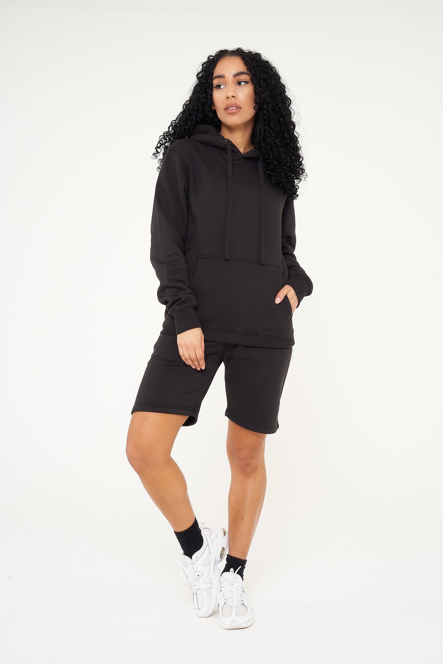 A woman in a black basic hoodie paired with shorts, standing in a casual pose.