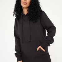 Woman wearing a basic black hoodie and shorts, front view, hands in pocket.