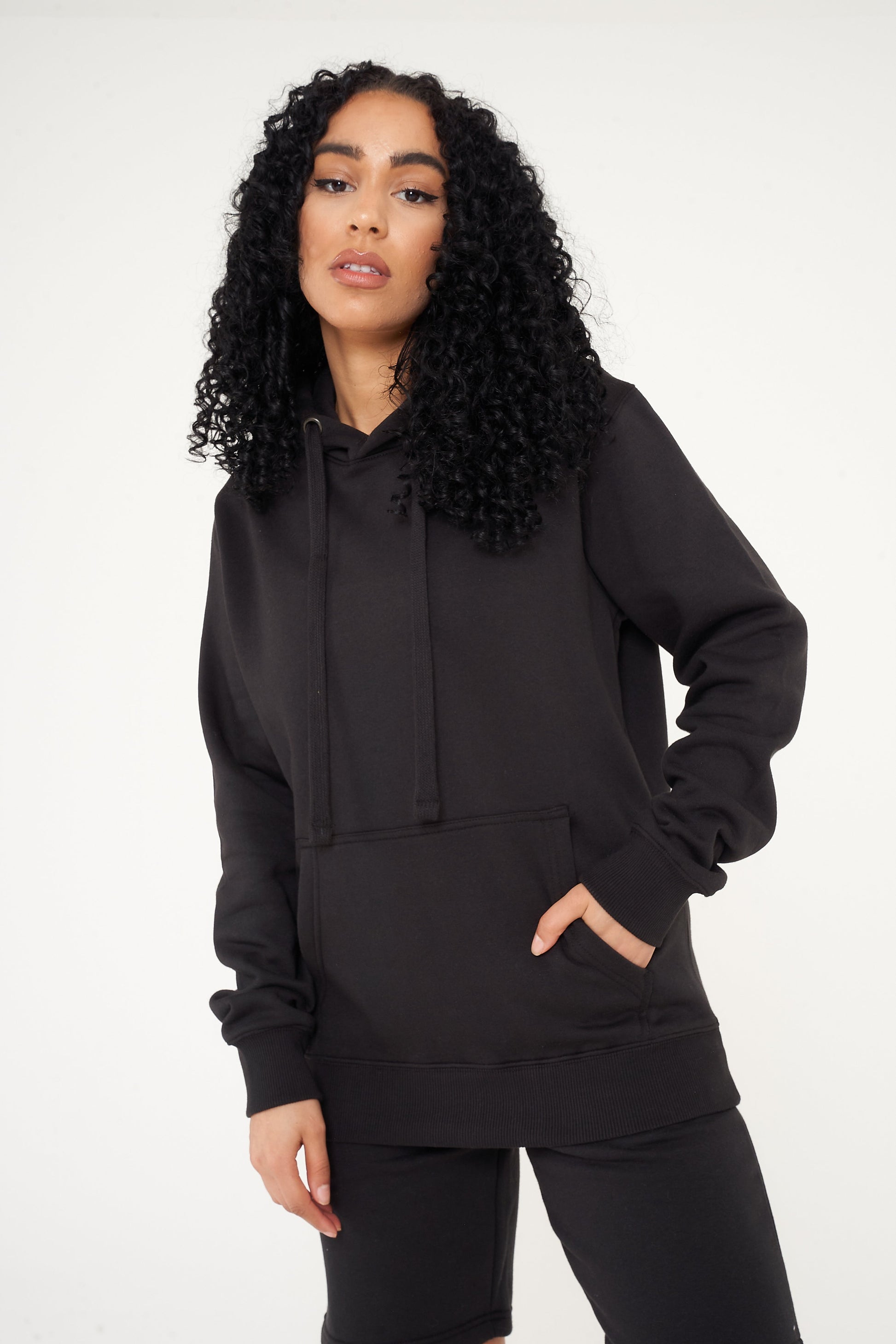 Woman wearing a basic black hoodie and shorts, front view, hands in pocket.