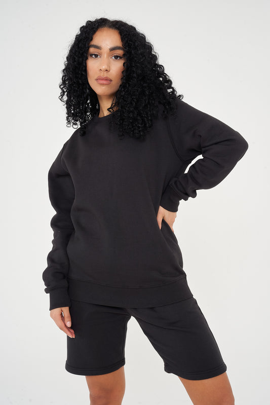 A woman wearing a black basic sweatshirt and black shorts, standing front-facing.