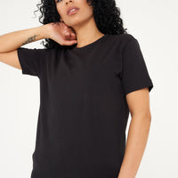 A woman standing in a black t-shirt and shorts, displaying effortless everyday style. 