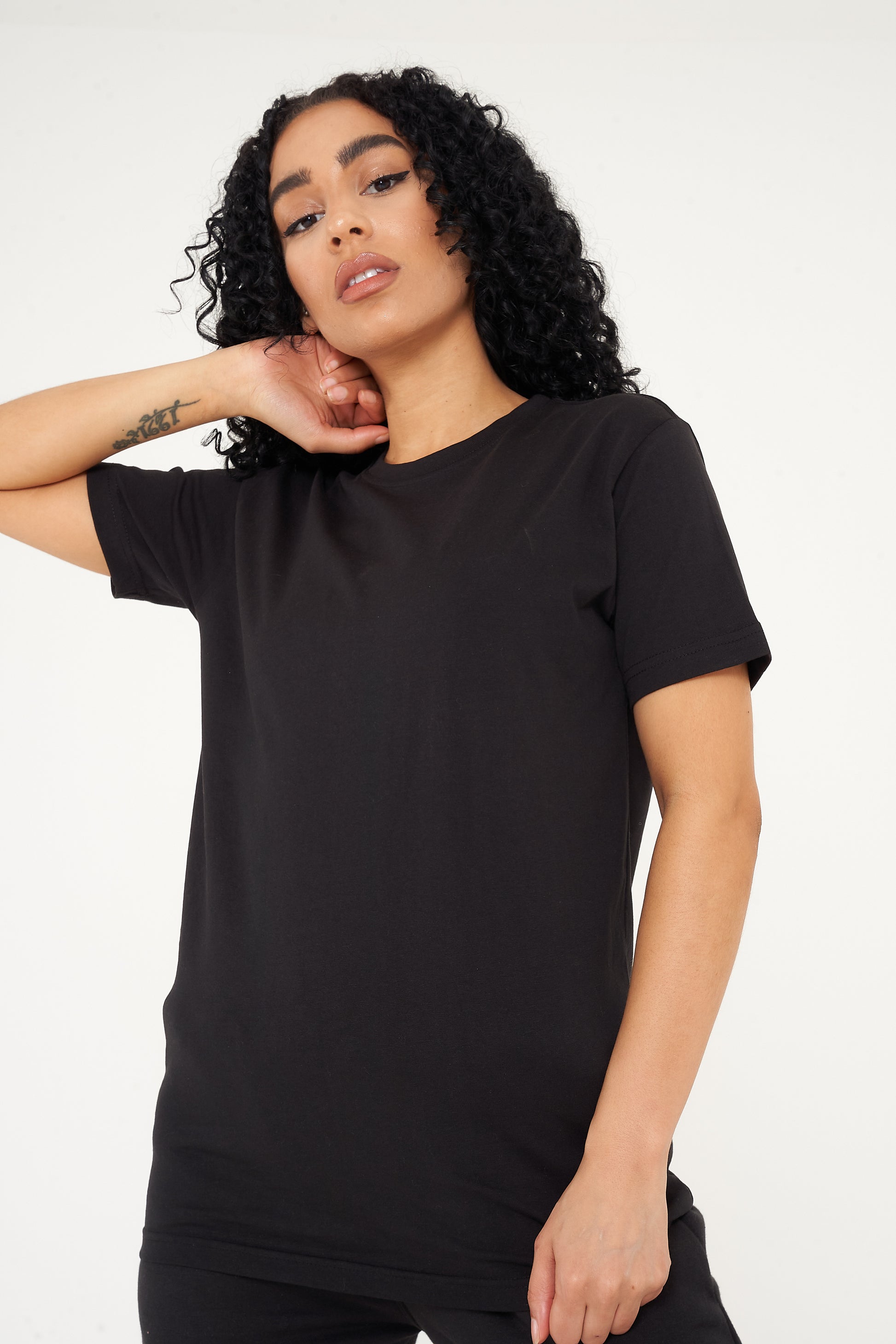 A woman standing in a black t-shirt and shorts, displaying effortless everyday style. 