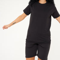 A woman dressed in a black t-shirt and shorts, in a casual pose to showcase fit and comfort. 