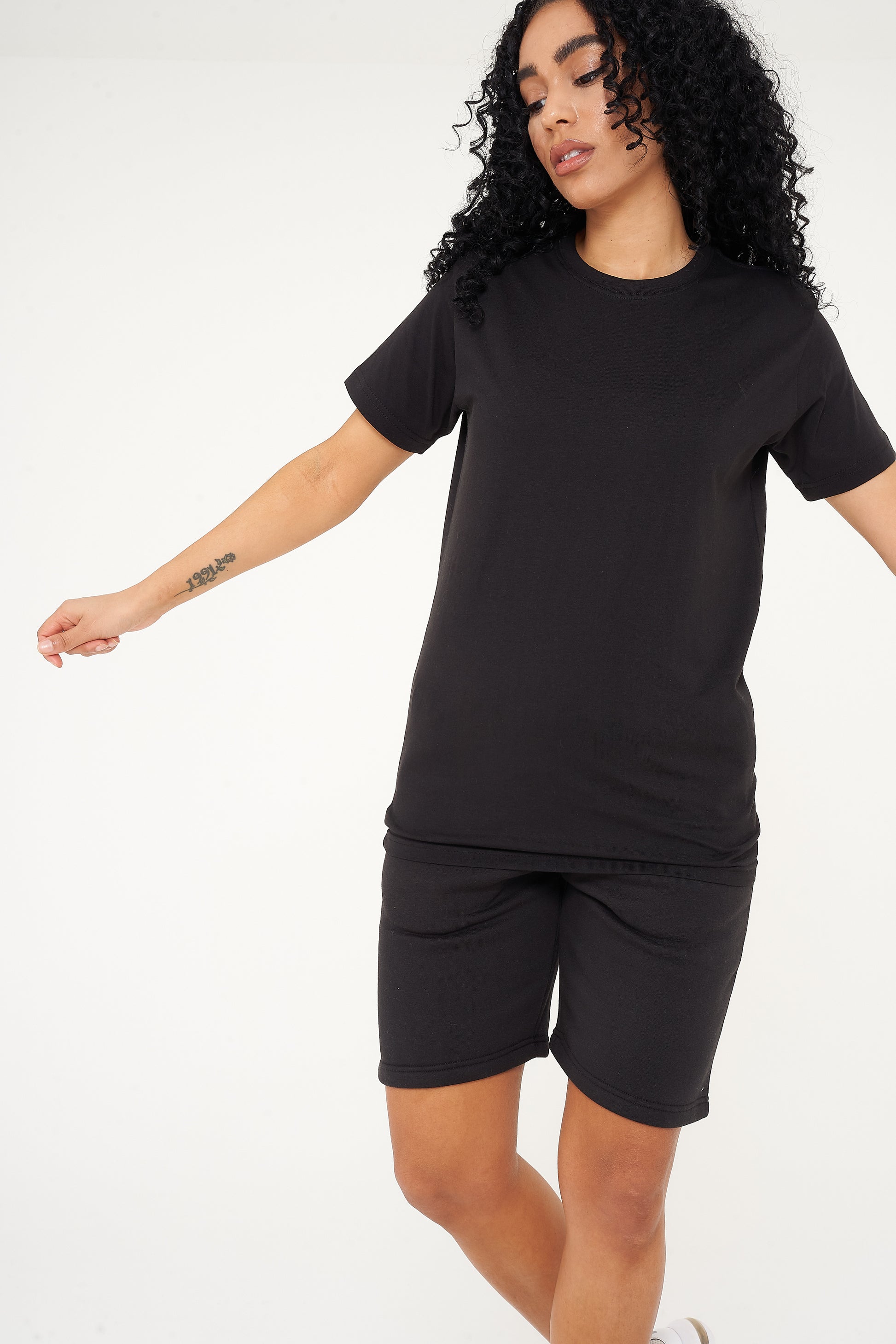A woman dressed in a black t-shirt and shorts, in a casual pose to showcase fit and comfort. 