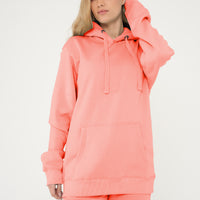 Woman standing in a basic coral hoodie and shorts, showing the hood and casual styling.
