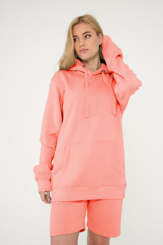 Woman standing in a basic coral hoodie and shorts, showing the hood and casual styling.