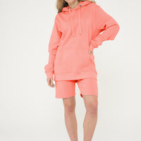 Woman wearing coral hoodie and matching shorts, front-facing, hands at sides.