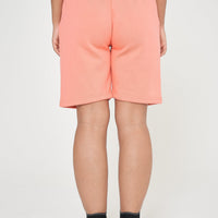 Woman in coral shorts and a matching t-shirt, sitting relaxed in a casual style pose.