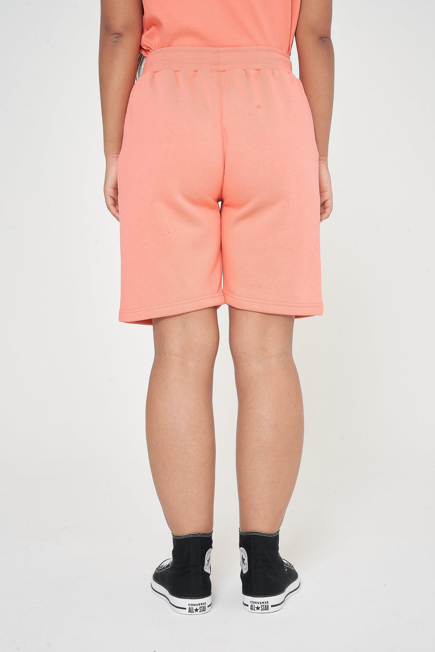 Woman in coral shorts and a matching t-shirt, sitting relaxed in a casual style pose.