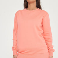 Woman standing in a coral sweatshirt and shorts, casual pose showcasing color and minimalist design. 