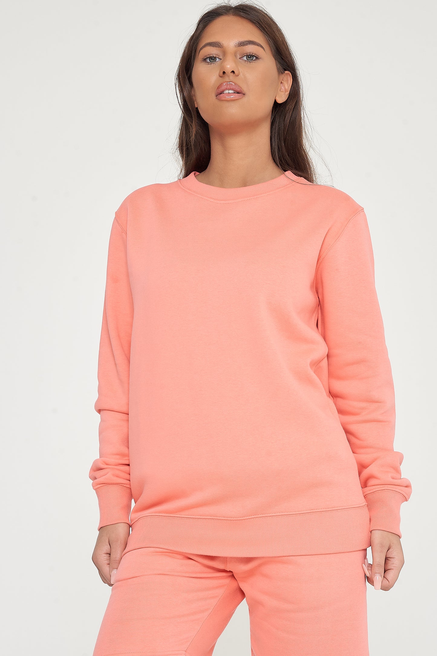 Woman standing in a coral sweatshirt and shorts, casual pose showcasing color and minimalist design. 
